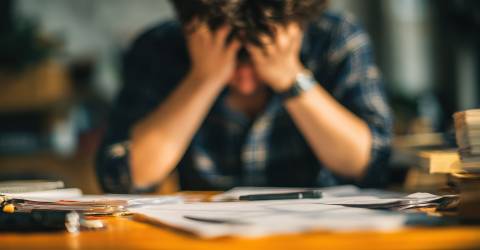 stress; man zit met handen op zijn voorhoogd achter zijn bureau